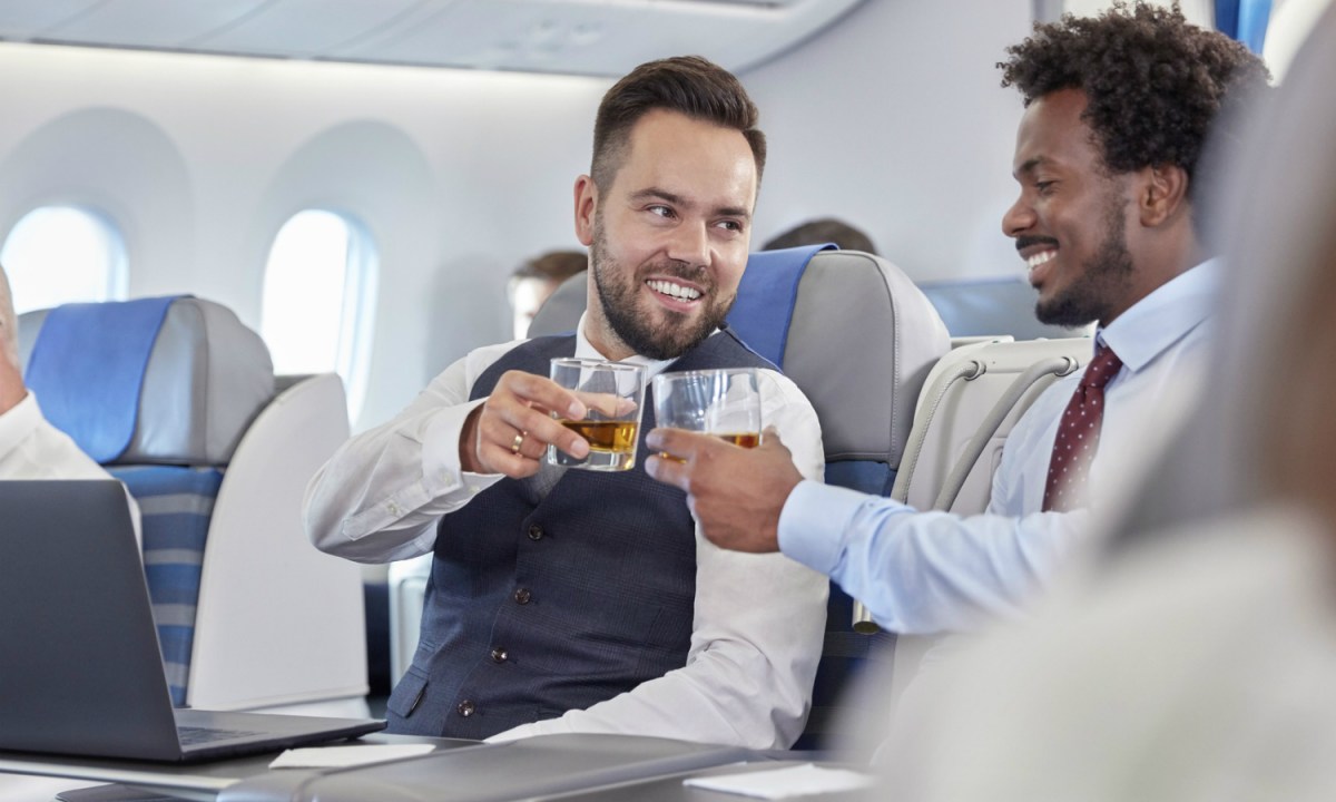 two men on an airplane cheersing with drinks