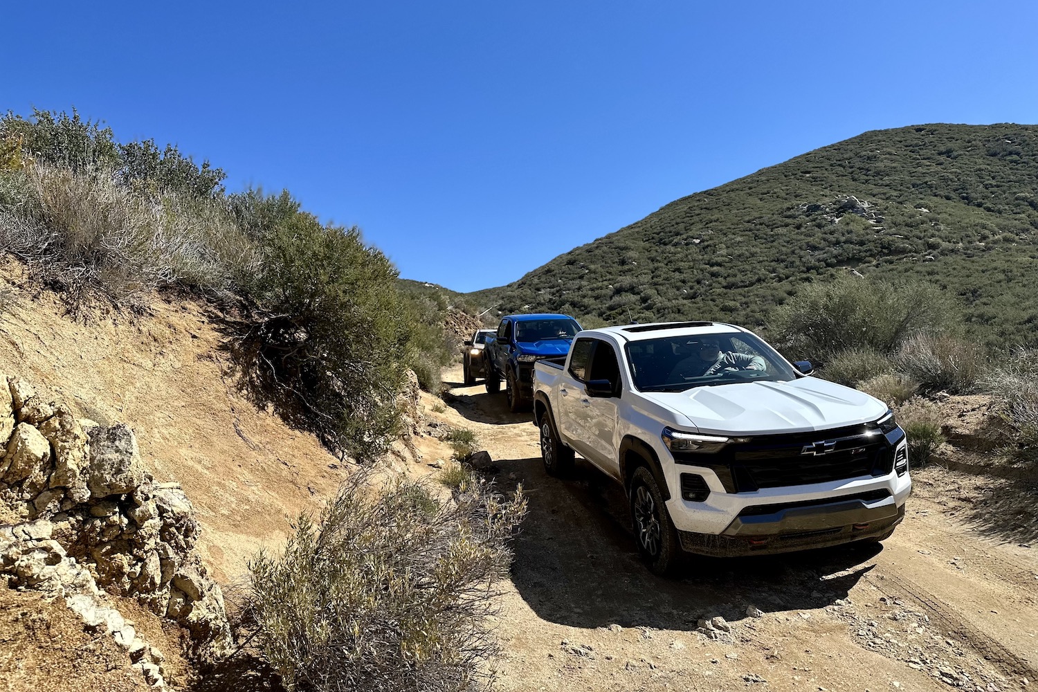 2023 Chevrolet Colorado Z71 front end angle off-roading on a dirt trail with mountains in the back.