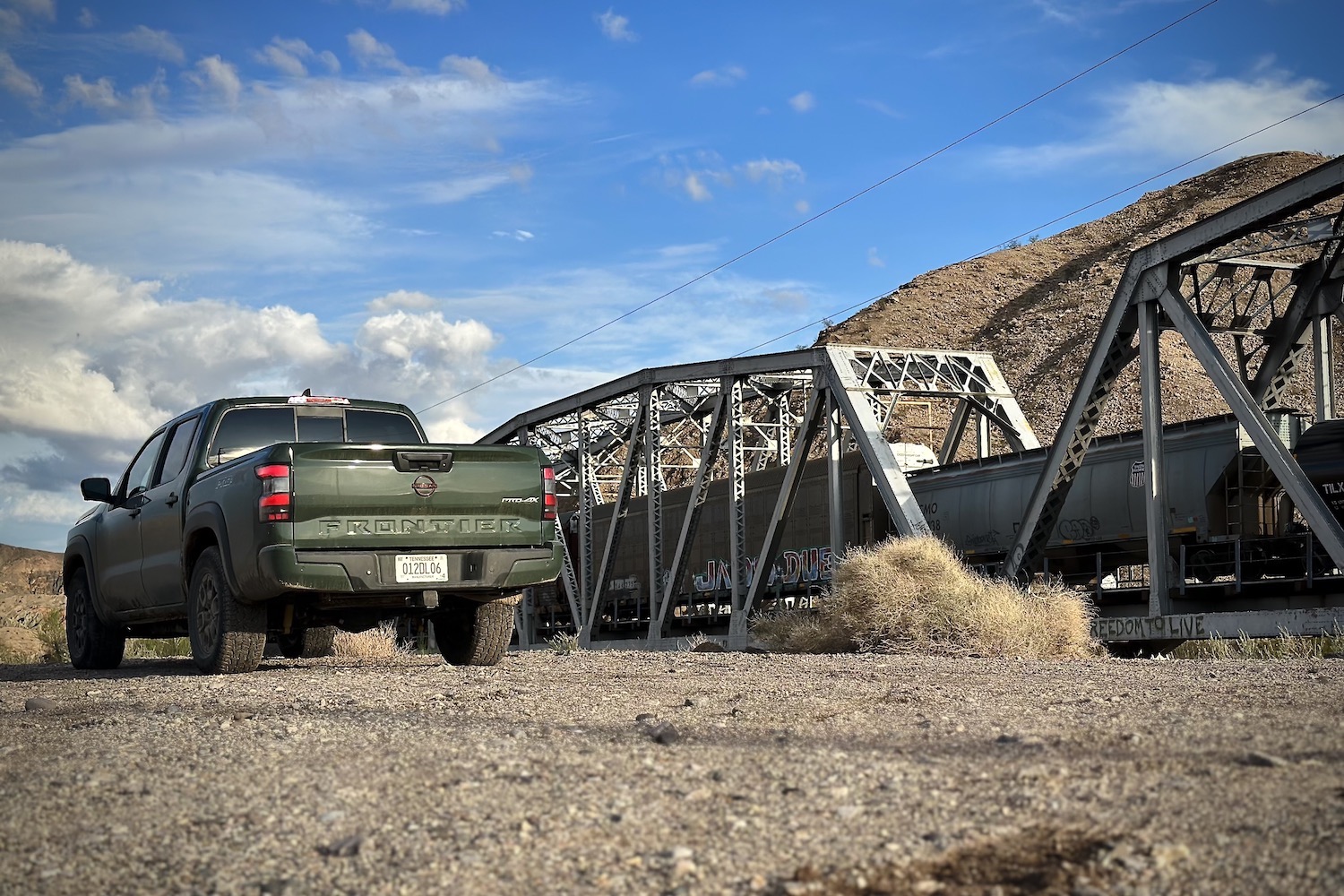 Rear end angle of the 2022 Nissan Frontier Pro-4X in front of a trail on a railroad track.
