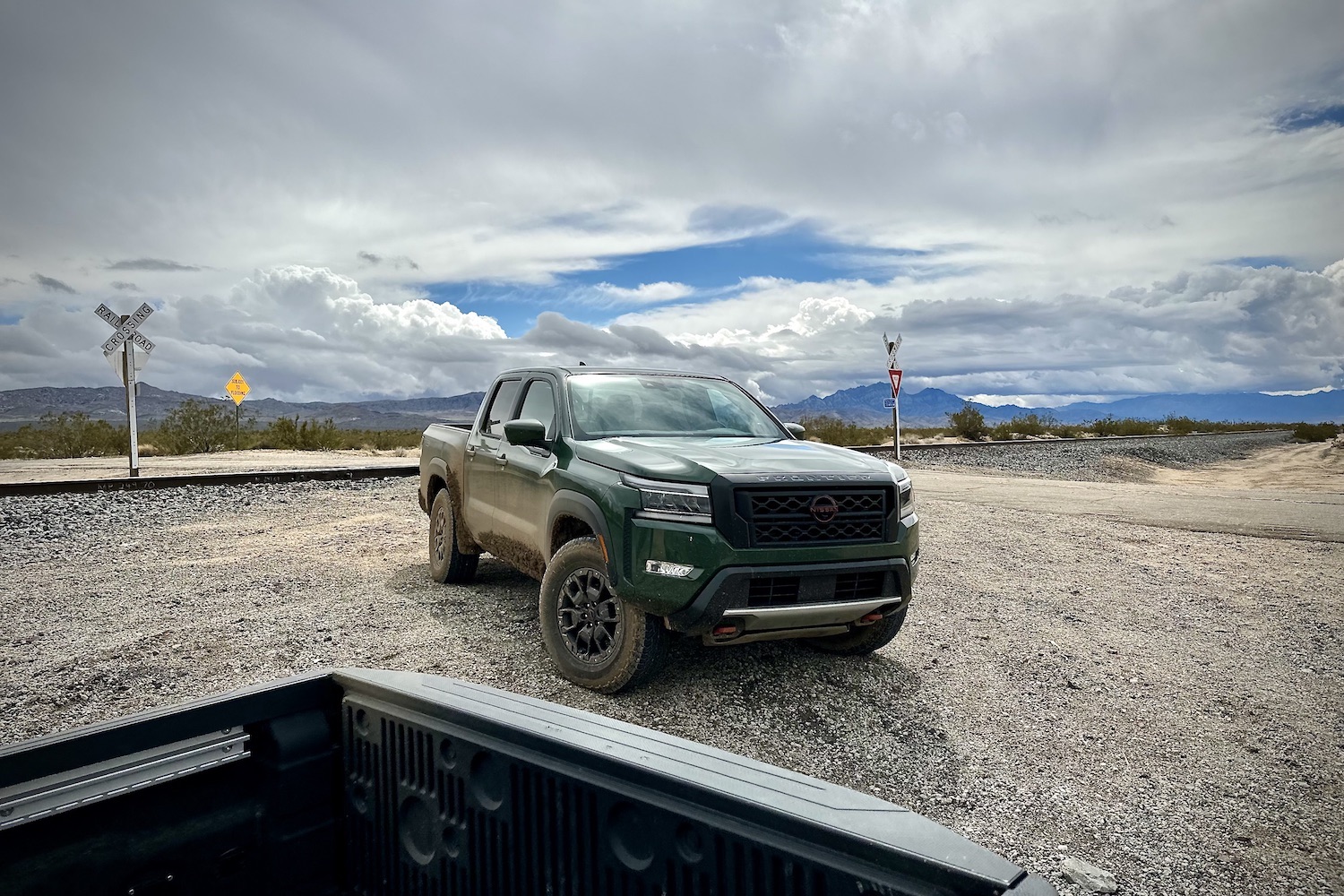 Close up of front end of the 2022 Nissan Frontier Pro-4X in front of mountains and clouds.