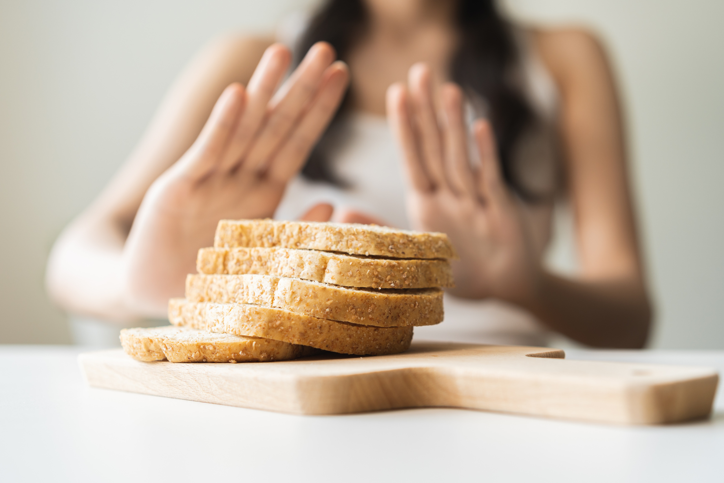 Woman with hands pushed out, refusing to eat white bread slice on chopping board