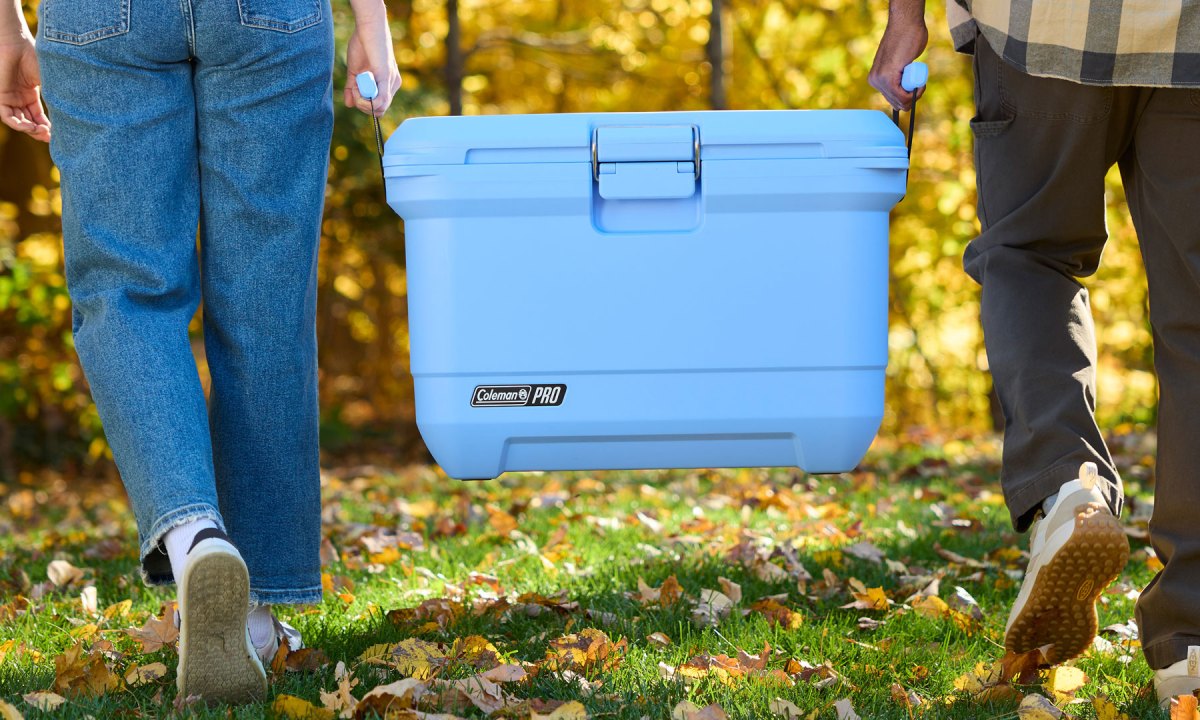 Coleman Pro 55-quart hard-sided cooler being carried by a couple in a field.